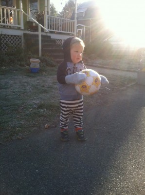 Lijah in pjs and sweatshirt holding a soccer ball in front of the house