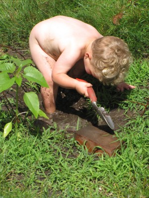 naked Lijah standing in a mud puddle with a trowel
