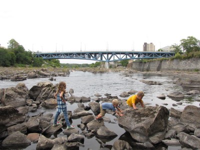 Harvey, Zion, and Havana clambering on rocks on the edge of the Merrimack River in Lowell