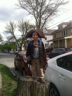 Zion in a pirate costume standing atop a stump next to the sidewalk