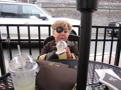 pirate Harvey sitting at an outdoor restaurant table, with a cup of lemonade clutched in his hook