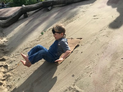 Lijah sliding down the sandy concrete slope at the Kemp Playground, wearing and eye patch