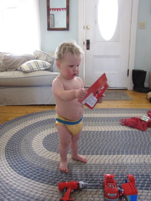 Lijah in just a diaper looking at a birthday card, new toys at his feet