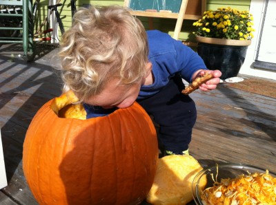 Lijah, cookie in his other hand, reaching deep into the pumpkin to pull out some goop
