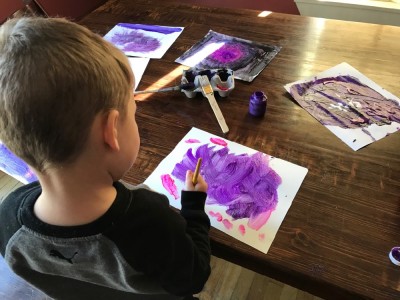Lijah painting purple art at the kitchen table
