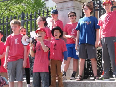 a group of kids in red shirts chanting on the State House steps