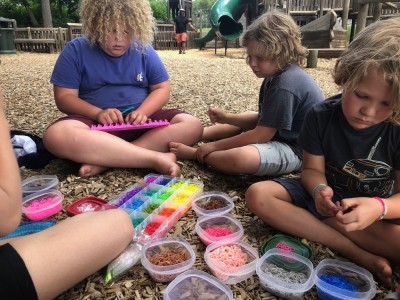 the boys making bracelets with little colored rubber bands on a playground