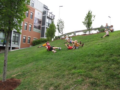 kids and a parent rolling down a steep grassy bank