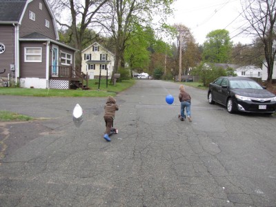 Zion and Harvey scootering down the street with balloons streaming out behind