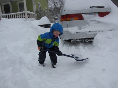 Zion shoveling in the driveway with the snow-covered car behind him