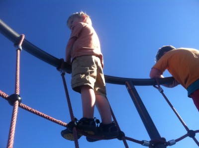 Zion (in shorts) at the top of a climbing structure against the blue sky