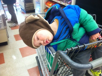 Lijah in monkey hat sleeping slumped over in the grocery store cart