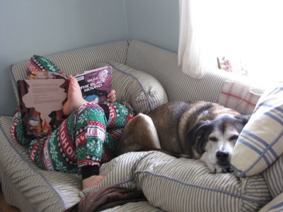 Harvey in PJs reading on the couch, Rascal cuddled on his feet