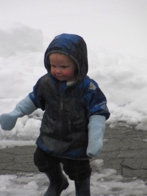 zion playing in the snowy street wearing raincoat and mittens