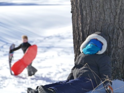 sledding: Lijah resting by a tree, Harvey coming up the hill behind him