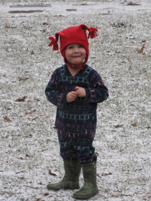 Lijah in PJs, hat, and boots, on the snowy lawn