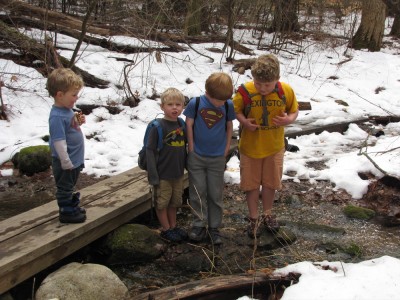 Harvey, Zion, Lijah, and Nathan posing crossing a stream in the snowy woods