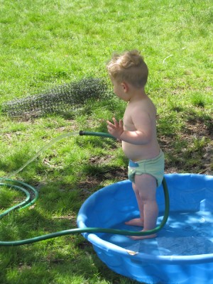 Lijah standing in the wading pool with a hose