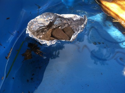 a boat molded out of tinfoil floating, supporting several rocks
