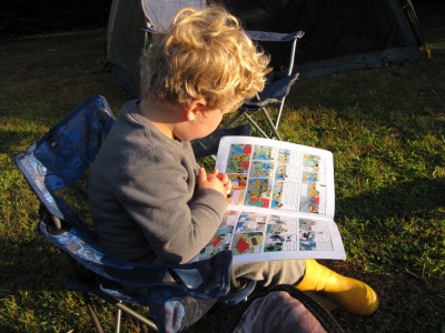 Harvey in his camping chair reading a Tintin book in the early morning sunlight