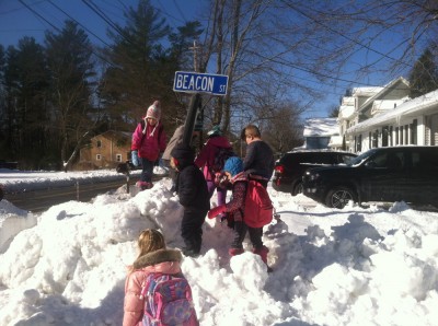 every kid at the bus stop climbing a mountain of snow to touch the street sign