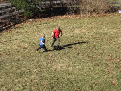 Harvey and Zion, in short sleeves, playing soccer in the snow-free yard