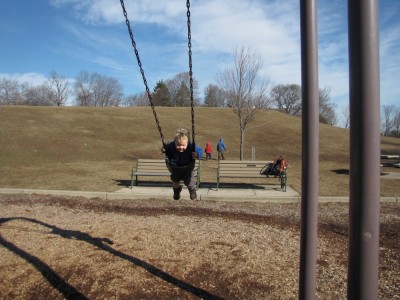 Lijah swinging high in the baby swing, brothers heading up a hill behind him