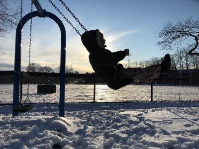 Lijah swinging at the playground with the low sun behind him