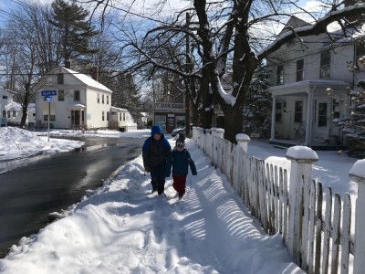 Harvey and Zion walking on the snowy sidewalk by a white picket fence