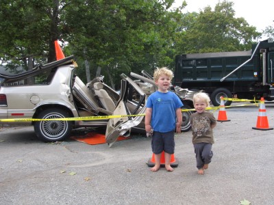 Harvey and Zion saying cheese in front of a car destroyed in a life-saving demonstration