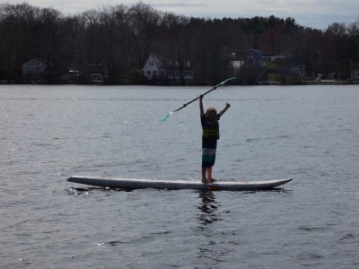 Zion raising his arms triumphantly standing on the windsurfer board in the pond