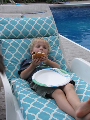 Zion relaxing in a chair by the pool eating a hamburger