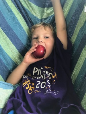 Lijah in the hammock chair biting a shiny apple