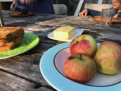 apples in a bowl on the outside table, next to a plate of french toast
