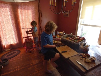 Zion cutting up apples at the kitchen table, Elijah turning the press behind him