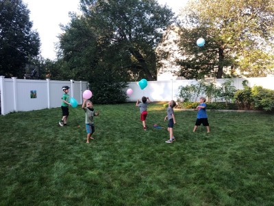 the boys and friends batting balloons in the air at a backyard party