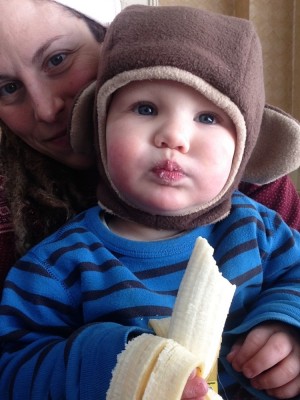 Leah holding Lijah, who's wearing a monkey costume hat and eating a banana