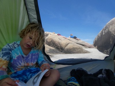 Elijah reading in our beach tent, his brothers lying on a rock outside drawing