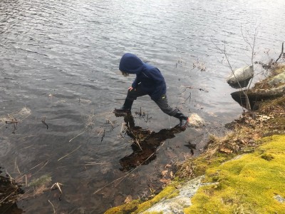 Elijah taking a big step onto a rock in a pond