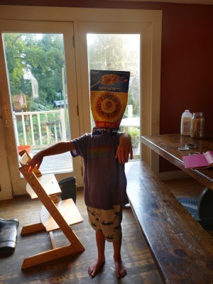 Elijah making a zombie pose with a cereal box over his head and face