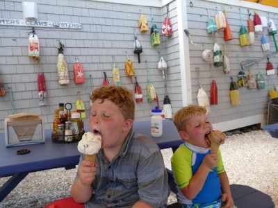 Harvey and Zion licking ice cream cones in front of a wall decorated with buoys