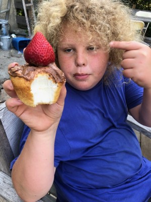 Harvey holding up a choco-frosted cupcake topped with a strawberry
