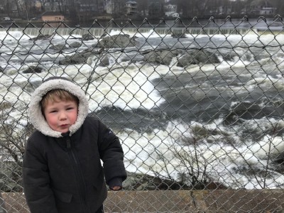 Lijah in snow coat alongside the wild waters of the Merrimack River