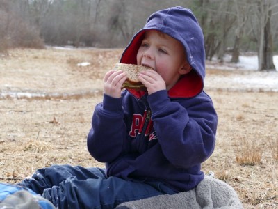 Zion biting into a sandwich picnicking in a field