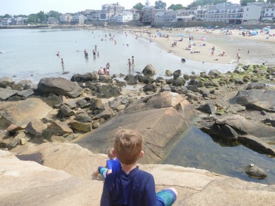 Elijah looking down from some rocks on to a crowded beach