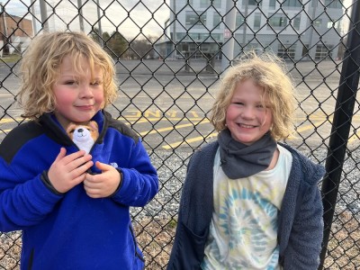 Zion (with a toy puppy in his shirt) and Elijah smiling in front of a chain link fence