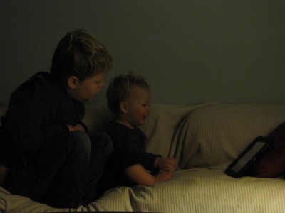 Harvey and Lijah on the couch in the dark, looking at the iPad