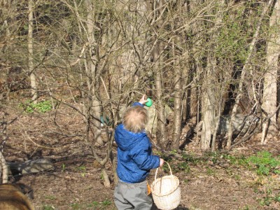 Zion, in winter coat, reaching into a bush to get an egg