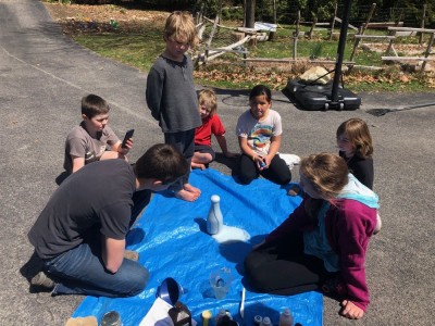 kids sitting around a tarp watching blue foam come out of a bottle