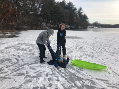 two big kids dragging Elijah by the legs on the ice